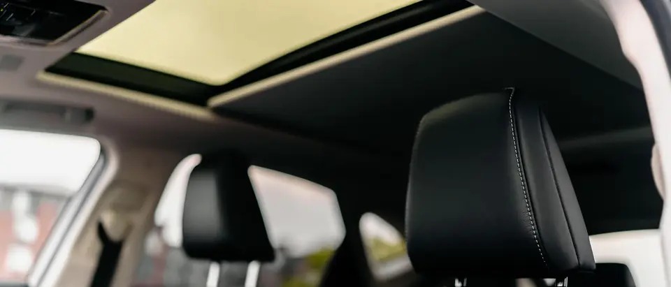 Black leather front seats of a car under an open glass panel overhead